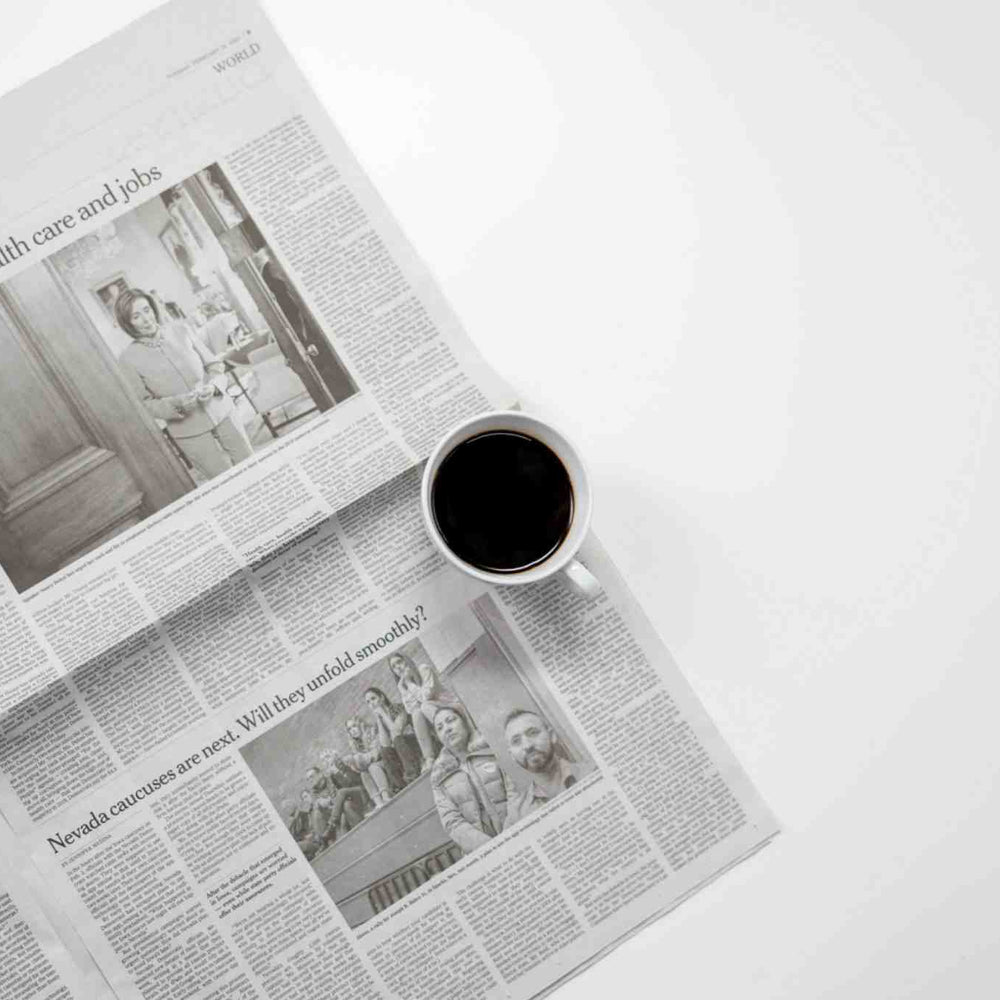 Ein minimalistischer Bildausschnitt einer Zeitung, bei dem eine Espressotasse in der Mitte des Bildes auf einer weißen Fläche liegt.